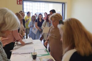 A group of people is lined up at a table, engaging with staff and handling papers in a bright, open space.