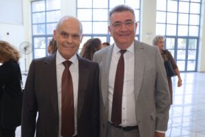 Two men in formal attire smile for the camera in a bright, spacious indoor setting.