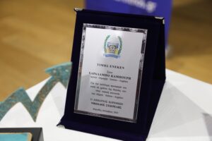A framed award plaque displayed on a table, featuring a decorative border and text in Greek.