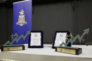 Two awards with figures climbing a graph, displayed alongside certificates, set against a blue backdrop.