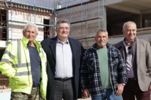 Four men pose together at a construction site, with scaffolding and building materials in the background.