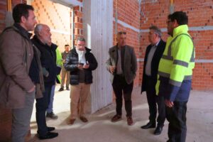 A group of men in a construction site, some in safety vests, discussing plans amidst brick walls.