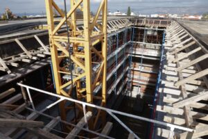 A construction site featuring a deep excavation with a yellow crane and wooden supports around the perimeter.