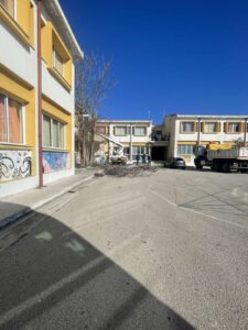 A view of a building complex with construction debris and a truck, under a clear blue sky.